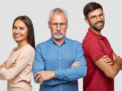 Self assured happy business partners stand backs, keep hands crossed, collaborate for developing own company. Positive woman, adult guy and senior man pose against white background. Relatives